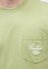 Ανοιχτό πράσινο βαμβακερό t-shirt με στρογγυλή λαιμόκοψη και κοντά μανίκια, με εμπρόσθιο τσεπάκι και λευκό κεντητό λογότυπο "Carhartt WIP".