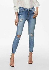 Tajta jeans i ljusblå denim med flera slitna områden och en femknapps-stängning. Accentuerade med en delad söm vid anklarna.