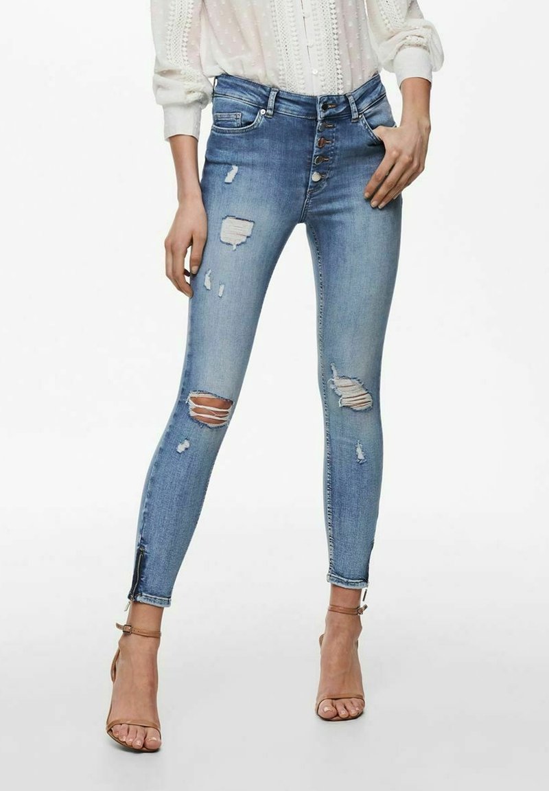 Tajta jeans i ljusblå denim med flera slitna områden och en femknapps-stängning. Accentuerade med en delad söm vid anklarna.