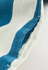 Gros plan sur un tissu rayé blanc et bleu sarcelle avec des coutures visibles le long du bord, montrant la texture et les détails des coutures.
