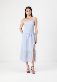 Vaaleansininen, hihaton maxi-mekko, jossa on istuva yläosa, tekstuuri-kangasta ja sivuaukko. Yhdistettynä violetit, remmillä varustetut korkokengät.