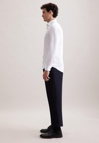 Camicia bianca con bottoni neri, abbinata a pantaloni blu navy e scarpe in pelle nere. Design elegante con una vestibilità su misura.