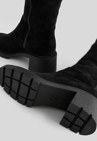 Bottes en daim noir mi-mollet avec talons blocs épais et semelles en caoutchouc robustes, avec fermetures éclair latérales et détail de semelle de marque.