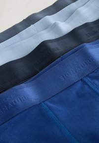 Cztery pary męskiej bielizny w różnych odcieniach niebieskiego. Każda z nich ma gładki pas z wytłoczonym napisem „NEXT SIGNATURE” w kontrastowym kolorze.