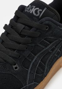 Sapatilha de camurça preta com parte superior texturizada, atacadores pretos e sola de borracha natural. Apresenta o logótipo na língua e acentos perfurados nas laterais.