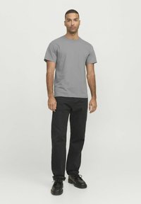 Camiseta gris de manga corta combinada con pantalones negros y zapatos de cuero negros. La camiseta tiene un cuello redondo y un diseño sencillo.