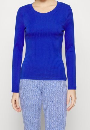 Haut ajusté bleu roi à manches longues côtelées, associé à un pantalon taille haute texturé bleu clair.