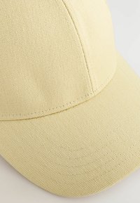 Geel canvas honkbalpet met een gestructureerde kroon, gebogen rand en gestikte details op het oppervlak. Over het algemeen heeft het een gladde textuur.