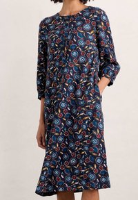 Vestido azul marino con un estampado floral que presenta acentos en rojo, azul y dorado. Escote redondo, mangas tres cuartos y bolsillos laterales.