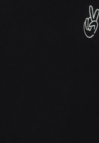 T-shirt nera in cotone con un gesto delle mani in segno di pace stampato in bianco sulla parte superiore sinistra. Design con scollo tondo e texture morbida.