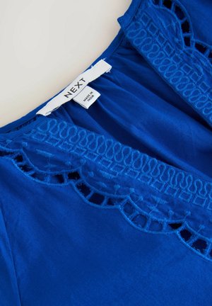 Niebieska bluzka z misternymi haftami wzdłuż dekoltu. Lekki materiał, luźny krój, z metką wskazującą markę "NEXT."