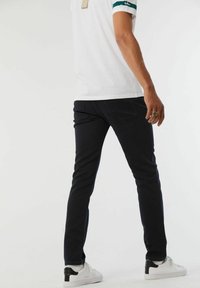 Jean skinny en denim foncé avec une texture lisse, associé à un t-shirt blanc avec des manches rayées vertes et des baskets noir et blanc.