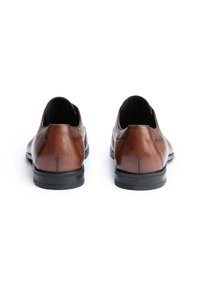 Paire de chaussures habillées en cuir marron avec semelles noires, vues de dos sur un fond blanc.