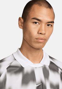 Nike polo shirt met een monochrome abstracte print, witte kraag, korte mouwen en textielstructuur. Logo aan de voorkant geplaatst.