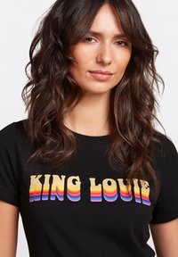 Camiseta negra con un audaz texto "KING LOUIE" multicolor en una fuente retro en capas. Tejido suave con un diseño clásico de cuello redondo.