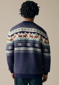 Pulover tricotat de culoare bleumarin, cu modele tematice de iarnă, reni, fulgi de zăpadă și copaci. Manșete și tiv cu bordură pentru o ajustare structurată.