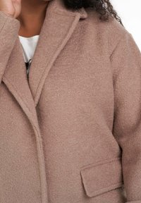 Blød, beige uldfrakke med notch-lapel, enkelt lomme og tekstureret overflade. Designet til komfort og varme.