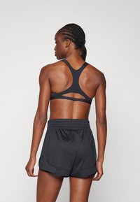 Zwarte sportbeha met een racerback design en een open uitsnijding; gecombineerd met zwarte shorts met elastische taille en zijzakken.