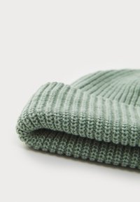 Strikket lue i lys grønn, med ribbestruktur, brettet brem og mykt garn. Fokuser på varmt materiale og praktisk design.