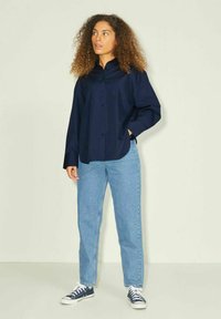 Camicia blu navy con colletto a punta, abbinata a jeans a vita alta azzurri e sneakers navy, caratterizzata da una vestibilità comoda e maniche lunghe.