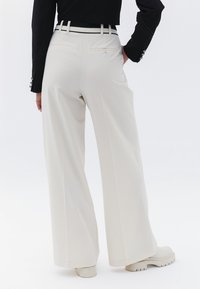 Szerokie spodnie w jasnym beżowym kolorze, z wysokim stanem, szlufkami na pasek, tylnymi kieszeniami i gładką fakturą. W zestawie z masywnymi białymi botkami.