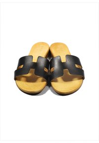 Sandali neri con due larghe cinghie dotate di intagli, posati su una soletta in beige chiaro e texturizzata. Suola piatta, design semplice.