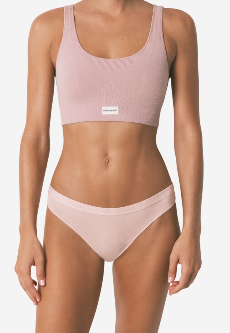 Světle růžový žebrovaný sportovní podprsenka s širokými ramínky a logem. Ladící světle růžové bikiny s měkkým pasem a minimálním zakrytím.