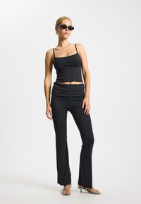 Zwart crop top met dunne bandjes en een aansluitend ontwerp, gecombineerd met zwarte flared broeken. Draag het met zilveren sandalen met bandjes en een zonnebril.