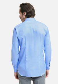 Camicia da uomo a maniche lunghe di colore azzurro chiaro, con colletto a punta, cucitura sul retro, e polsini con bottoni, realizzata in tessuto morbido.