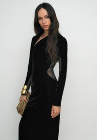 Melnas samta kleitas ar garām piedurknēm, kas izgatavotas no caurspīdīgas punktu acs. Kleita ir asimetriskā griezumā ar pieguļošu siluetu.