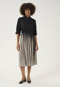 Čierne šaty s vysokým golierom a plisovanou sukňou v krémových a čiernych pruhoch. Mäkkučká látka, rukávy po tri štvrtiny a gombíková léga.
