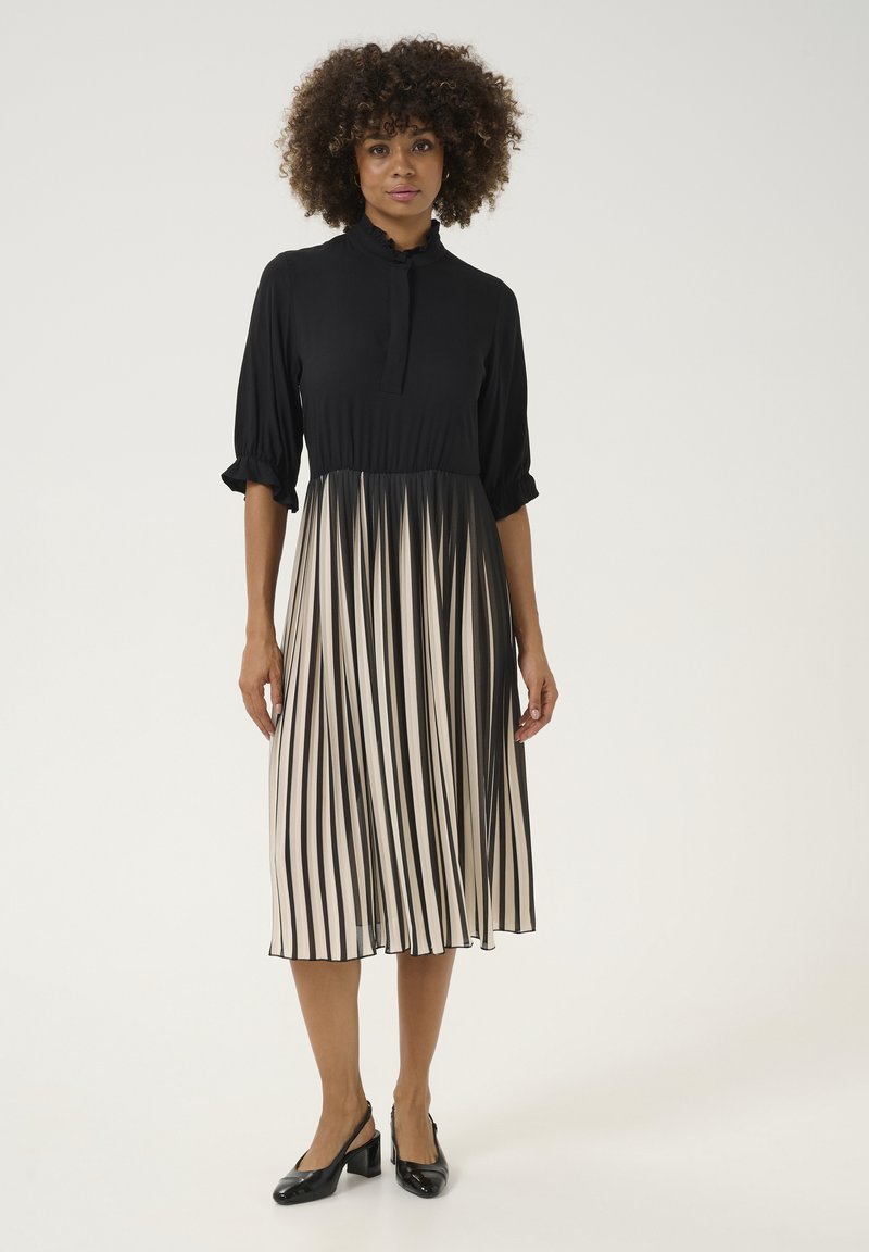 Čierne šaty s vysokým golierom a plisovanou sukňou v krémových a čiernych pruhoch. Mäkkučká látka, rukávy po tri štvrtiny a gombíková léga.