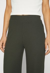 Mörkgröna ribbade loungebyxor med bred midja. Tyget har en mjuk textur och har vertikala ränder, vilket ger en åtsittande passform.