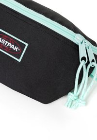 Estuche negro con una tela texturizada, con un zipper y cuerdas azul claro, y un parche de logo negro y rojo en el lateral.