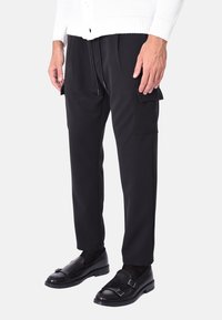 Pantaloni cargo neri con una vestibilità rilassata, dotati di tasche laterali, una texture liscia e un cordino elastico in vita. Indossati con scarpe nere.