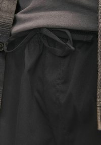 Svarta shorts med en strukturerad midja, med en inre dragsko. Tyget verkar slätt med en subtil glans, stoppad under en grå tröja.