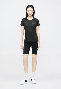 Zwart kort T-shirt met korte mouwen en zwarte fietsshort, gemaakt van gladde stof. Het T-shirt heeft een klein logo. Witte sneakers met zwarte accenten.