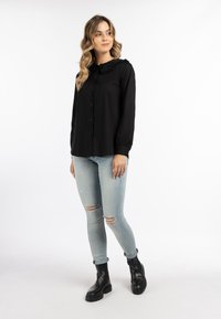 Schwarze Bluse mit Knopfverschluss und Rüschensaum, kombiniert mit hellblauen, zerrissenen Jeans und schwarzen Stiefeletten; glatte Stoffqualität und figurbetonte Passform.