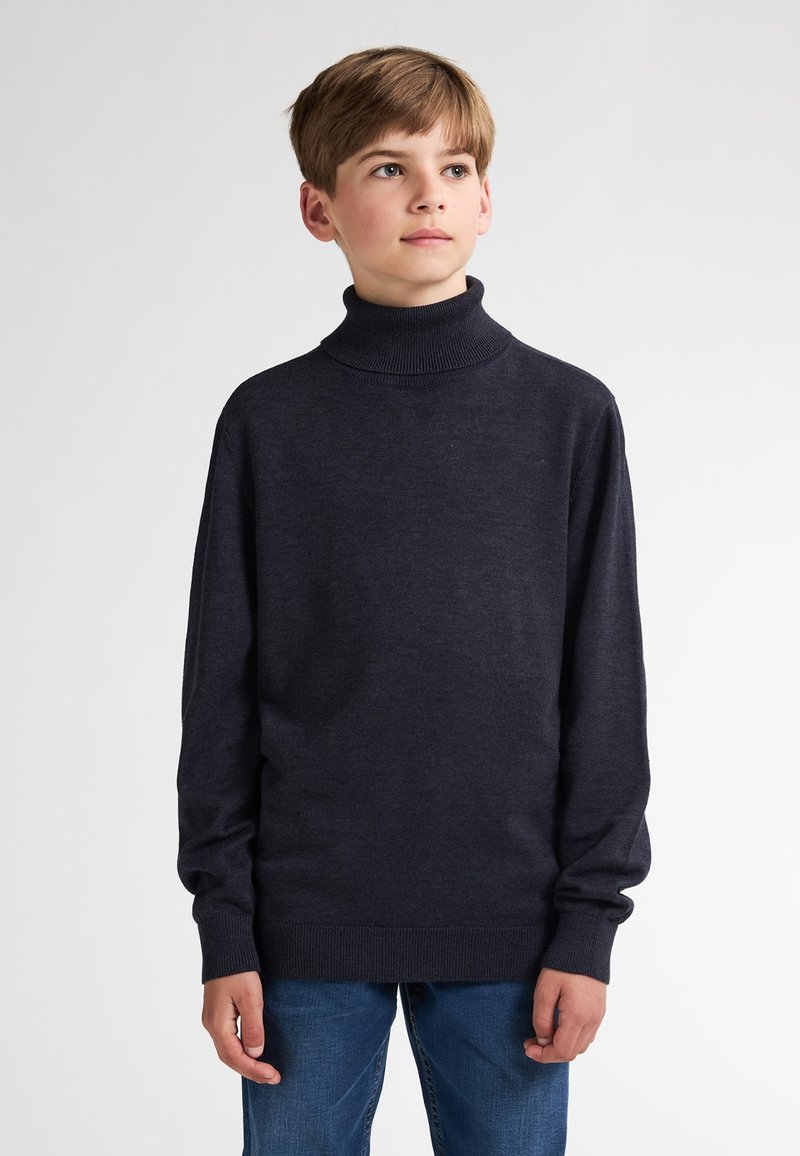 Dunkelblaues Rollkragenpullover aus Strickstoff mit langen Ärmeln und gerippten Bündchen. Kombiniert mit hellblauen Jeans. Glatte Textur.