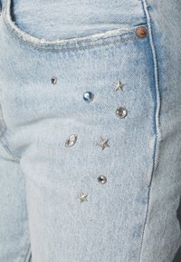 Ljusblå denimjeans med silver- och blå utsmyckningar, som har stjärnformer och olika rhinestones på framsidan.