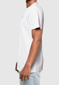 Valkoinen puuvillainen t-paita, jossa on lyhyet hihat, pyöreä kaula-aukko ja suora leikkaus. Edessä on tekstipainatus. Yhdistetty vaaleansinisiin farkkuihin.