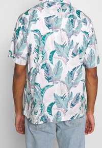 Kortärmad, lättviktig skjorta med en vit bas och ett flerfärgat bladmönster i grönt och rosa. Har en avslappnad passform och krage.