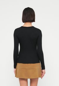 Μαύρο μακρυμάνικο τοπ με ριμπ υφή, εφαρμοστό σχέδιο. Συνδυάζεται με φούστα σε μπεζ χρώμα από κορντορού, με φαρδύ κάτω μέρος και εμφανείς ραφές.