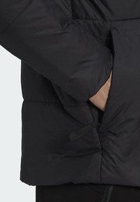 Giacca imbottita nera con colletto alto, dotata di tasca con zip laterale e coulisse elastica sull'orlo per la regolabilità.