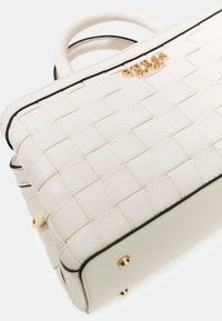 Sac à main tissé blanc avec un design structuré, accents noirs, texture lisse, ferrures dorées et détail du logo sur le devant.