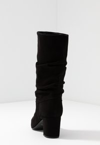 Czarne, luźne kozaki sięgające za kolano, wykonane z miękkiego zamszu, z grubym obcasem i teksturowanym cholewką. Gładkie wnętrze z minimalną widoczną metaloplastyką.