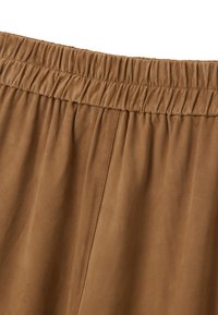 Détail de taille élastique marron en tissu doux et semblable à du suède. Présente une texture subtile et des coutures nettes sur le vêtement. Design lisse et fluide.