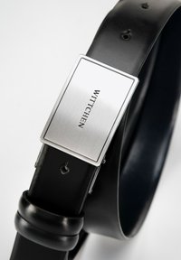 Cinturón de cuero negro con hebilla rectangular plateada grabada con "WITTCHEN", textura suave, agujeros para ajuste, diseño minimalista.