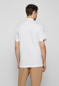 Camisa polo branca de manga curta, com um design liso e riscas de destaque nos punhos; feita de um tecido suave e texturizado.