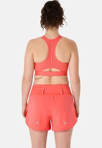 Coral sports bra and matching shorts, both featuring breathable fabric. The shorts have side slits and reflective accents for visibility.